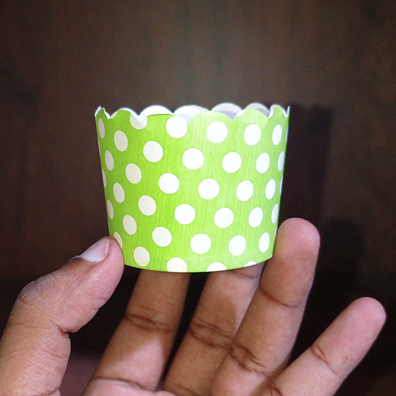 Green paper cupcake liner with white polka dots held in a hand against a dark background