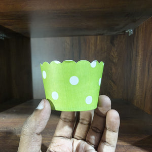 Hand holding a green paper cupcake liner with white polka dots against a wooden background