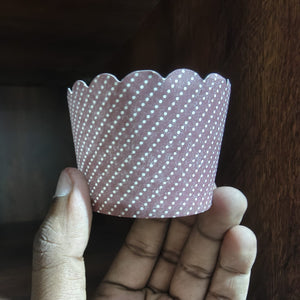 Hand holding a pink cupcake liner with white polka dots against a dark background