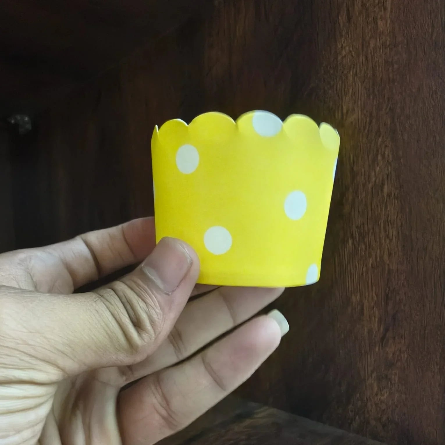 Hand holding a yellow paper crown with white polka dots against a wooden background