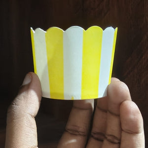 Hand holding a yellow and white striped paper cupcake liner against a dark background