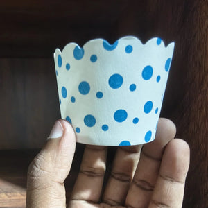 Hand holding a white paper cupcake liner with blue polka dots against a wooden background