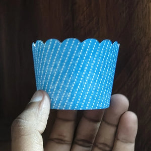 Hand holding a blue cupcake liner with white polka dots against a wooden background