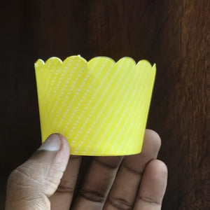 Hand holding a yellow scalloped-edge cupcake liner against a dark background