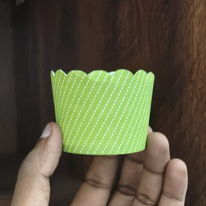 Hand holding a green cupcake liner with white polka dots against a wooden background
