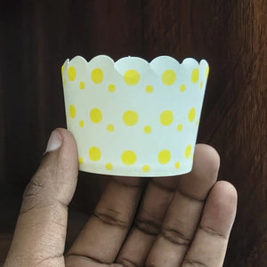 Hand holding a white cupcake liner with yellow polka dots against a dark background