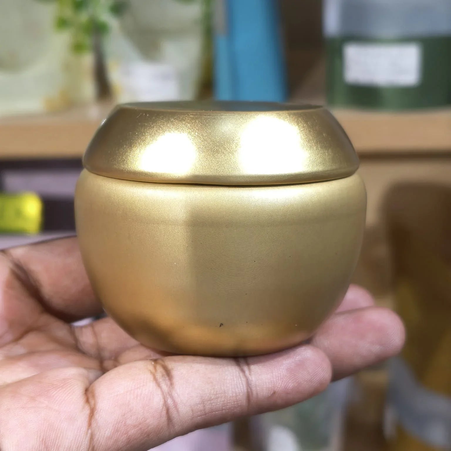 Gold-colored container held in a hand with a blurred background