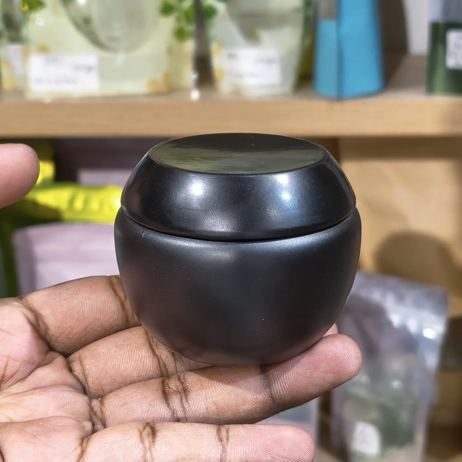 Black ceramic container held in a hand with a blurred background