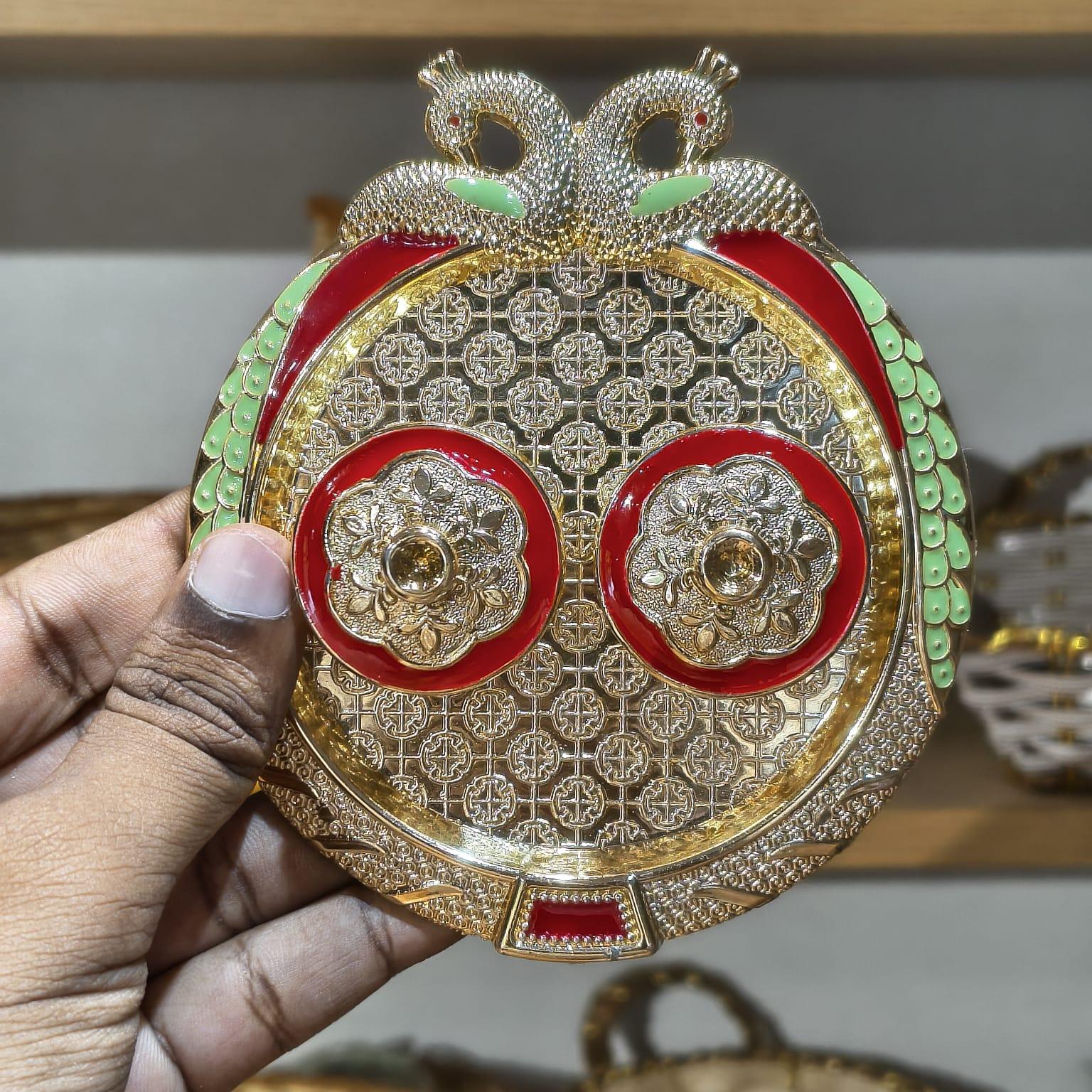 Decorative item with gold, red, and green colors held by a hand.