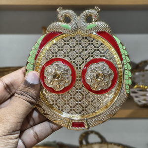 Decorative item with gold, red, and green colors held by a hand.
