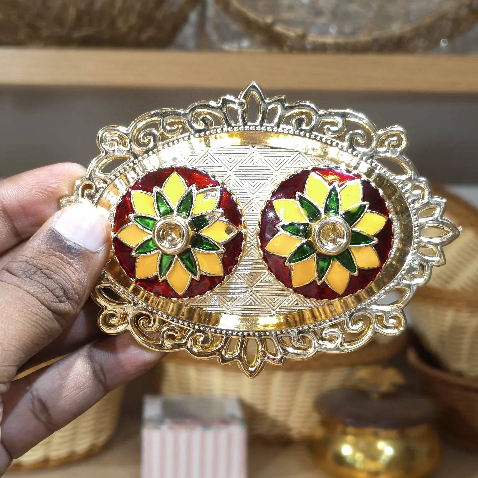 Decorative earrings with a gold and red design held by a hand.