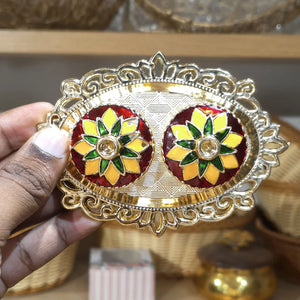 Decorative earrings with a gold and red design held by a hand.