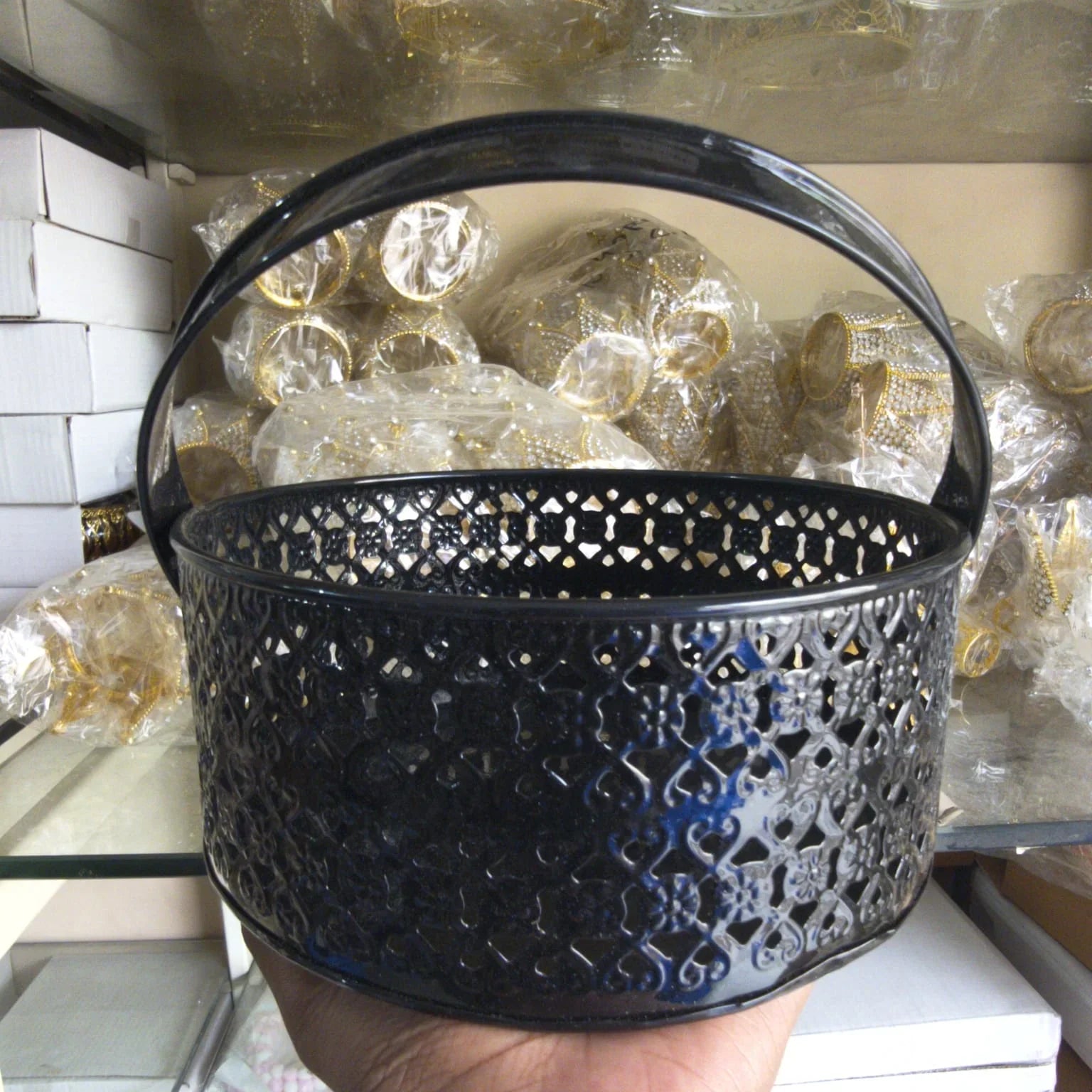 Black decorative basket held in front of a shelf with wrapped items