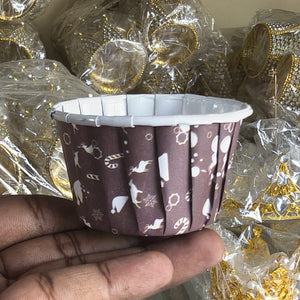 Hand holding a brown cupcake liner with white patterns against a background of wrapped items.