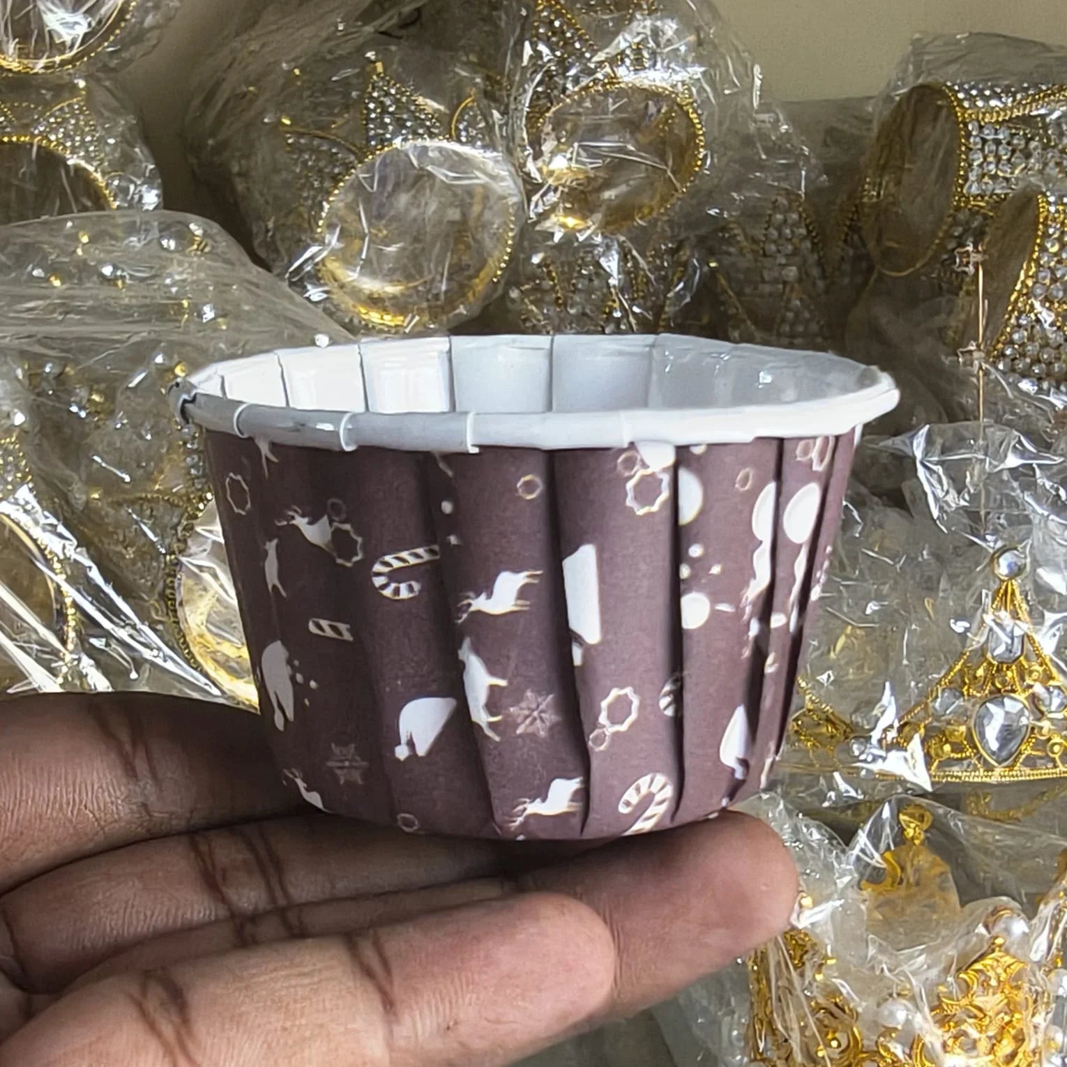 Hand holding a brown cupcake liner with white patterns against a background of wrapped items.