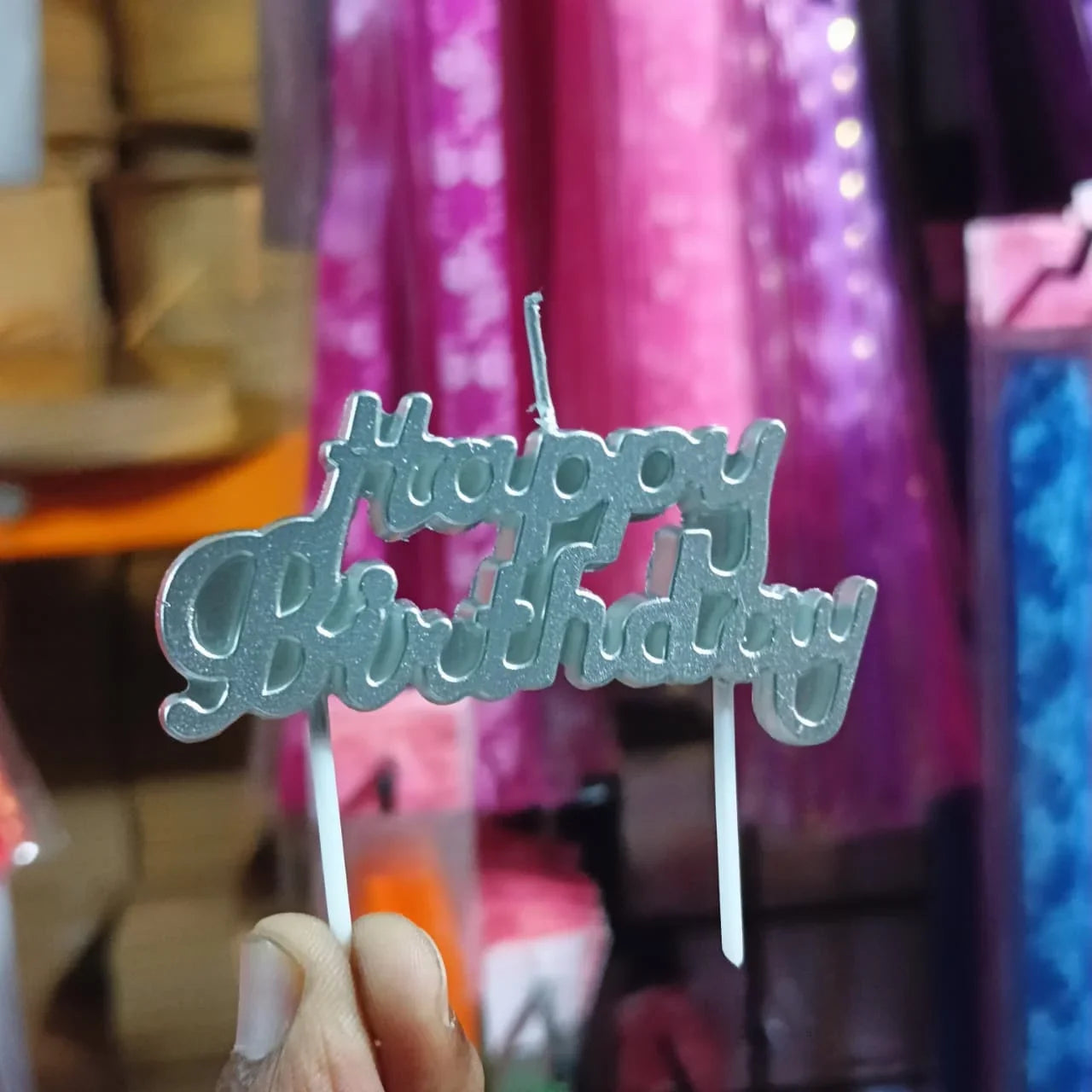 Metallic 'Happy Birthday' cake topper held in front of a colorful background