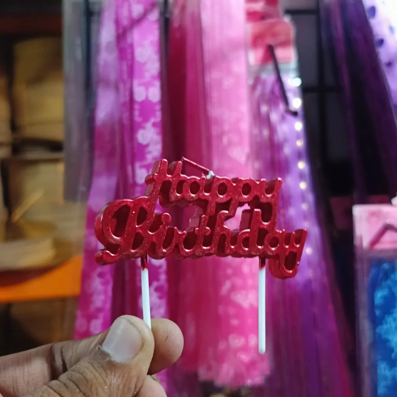 Red 'Happy Birthday' cake topper held by a hand with a blurred background