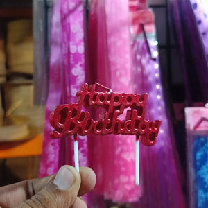 Red 'Happy Birthday' cake topper held by a hand with a blurred background