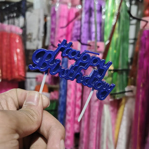 Blue 'Happy Birthday' cake topper held by a hand with colorful background