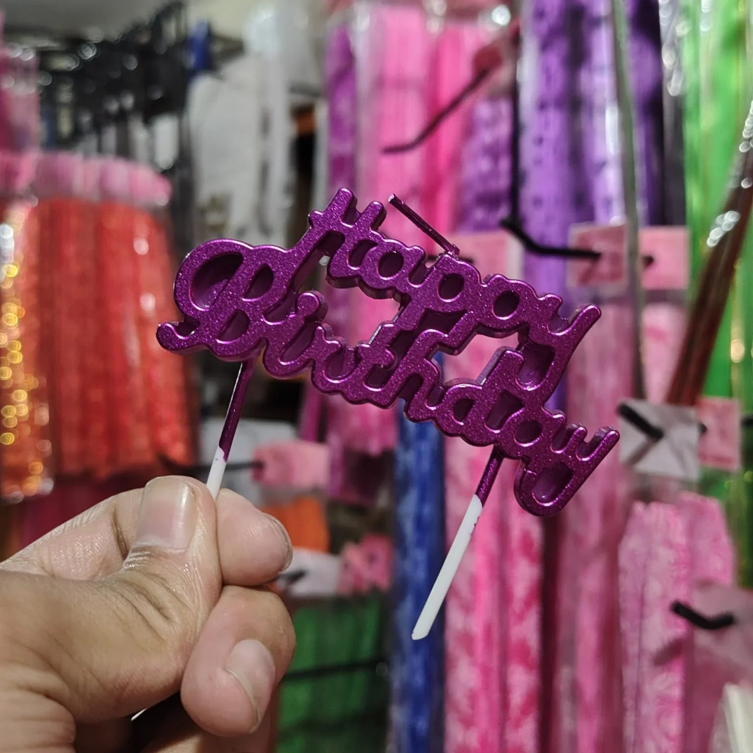 Purple 'Happy Birthday' cake topper held in front of colorful decorations.