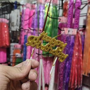 Gold 'Happy Birthday' cake topper held in front of colorful party supplies.