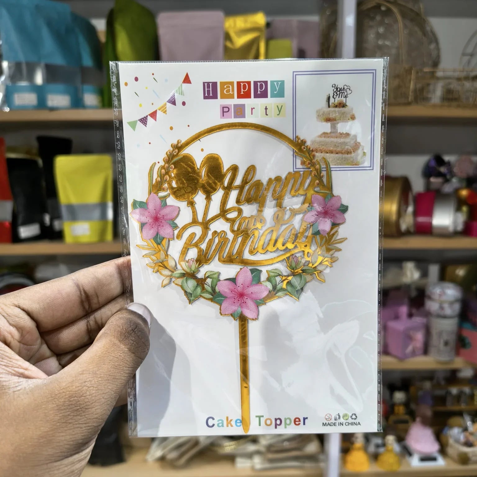 Hand holding a 'Happy Birthday' cake topper card with decorative elements.