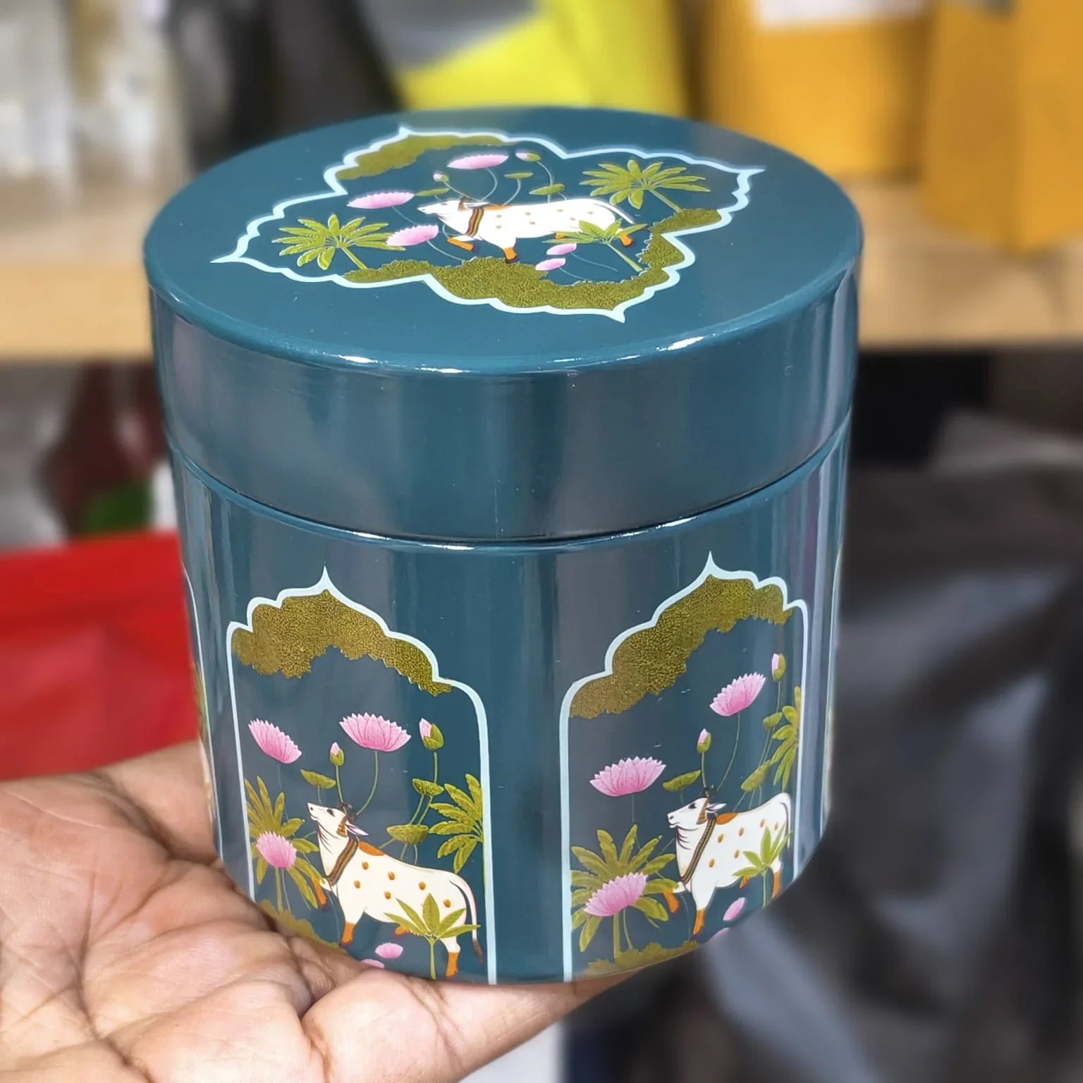 Blue cylindrical container with cow and flower design held by a hand