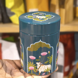 Teal cylindrical container with floral and animal design held by a hand