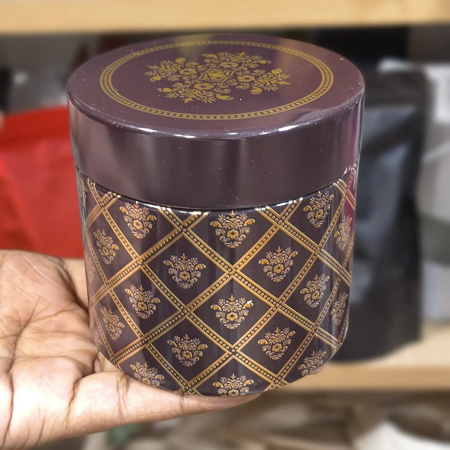 Decorative purple container with gold patterns held by a hand against a blurred background