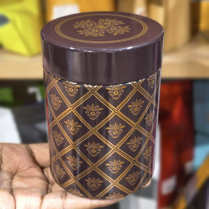 Decorative brown cylindrical container with gold patterns held by a hand against a blurred background.
