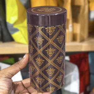 Cylindrical container with decorative gold patterns held by a hand against a blurred background