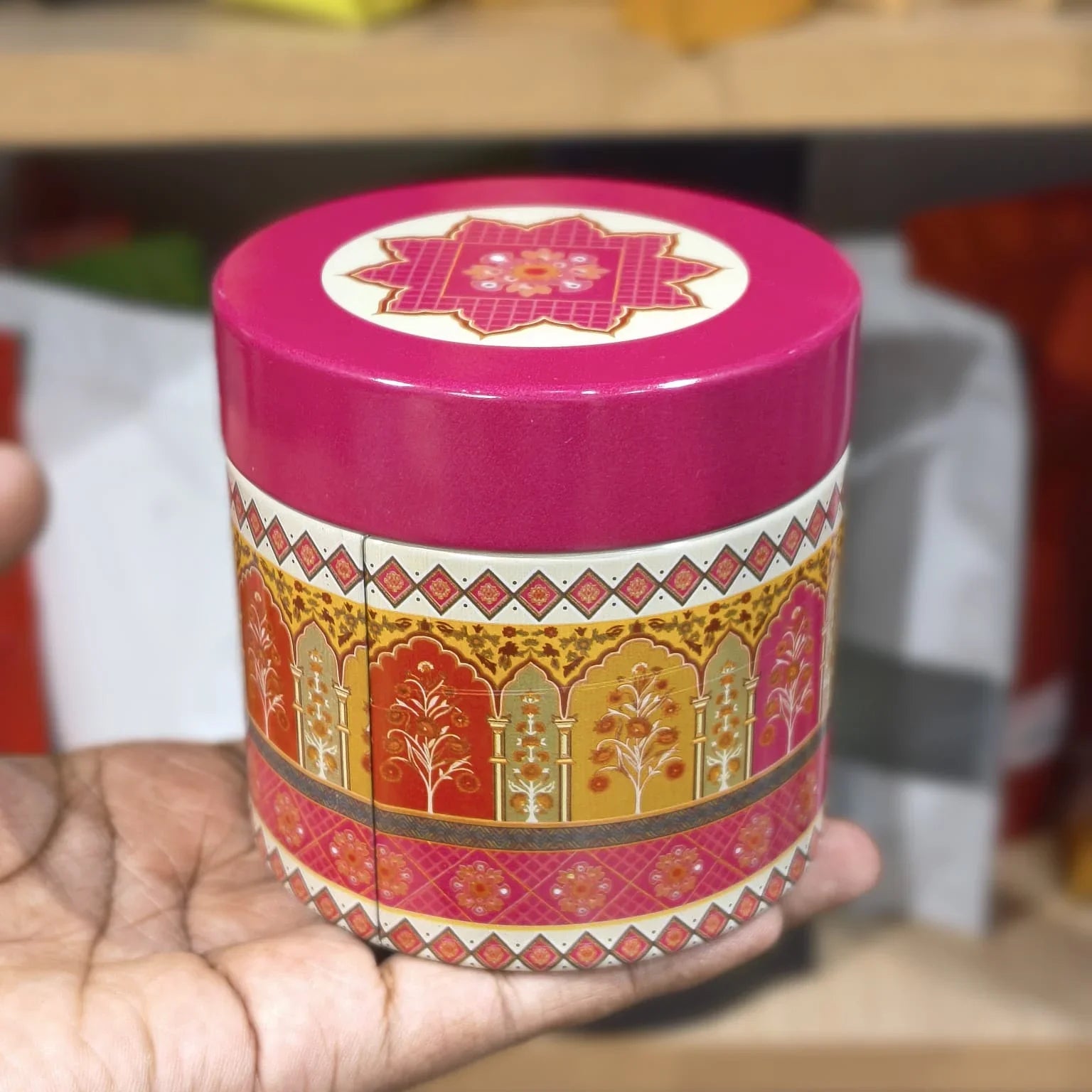 Decorative cylindrical container with a pink lid held in a hand against a blurred background