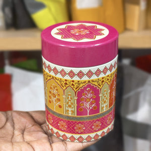 Decorative cylindrical container with pink lid and intricate patterns held by a hand.