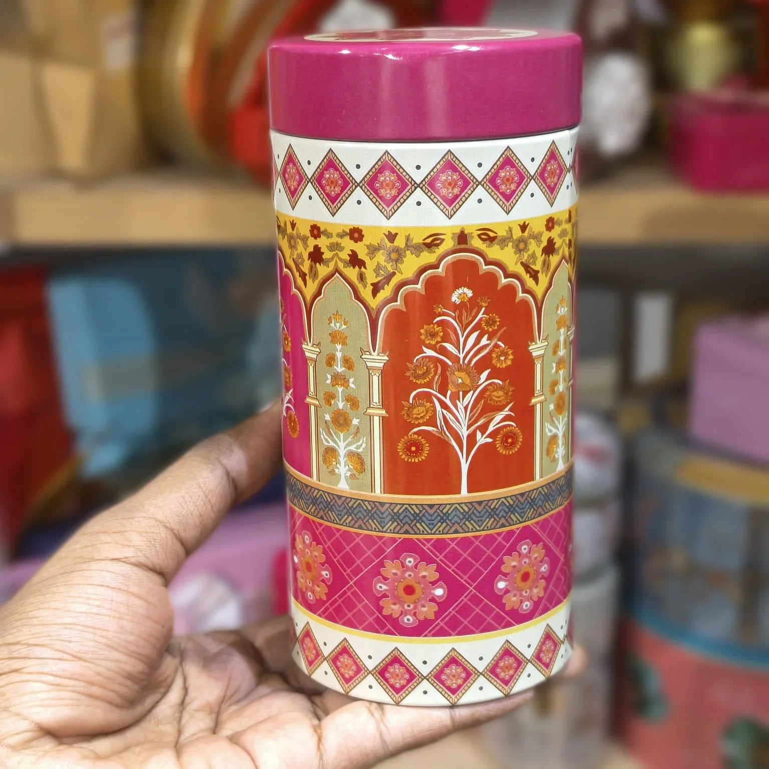 Decorative cylindrical container with intricate patterns held by a hand against a blurred background