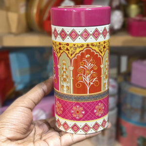 Decorative cylindrical container with intricate patterns held by a hand against a blurred background