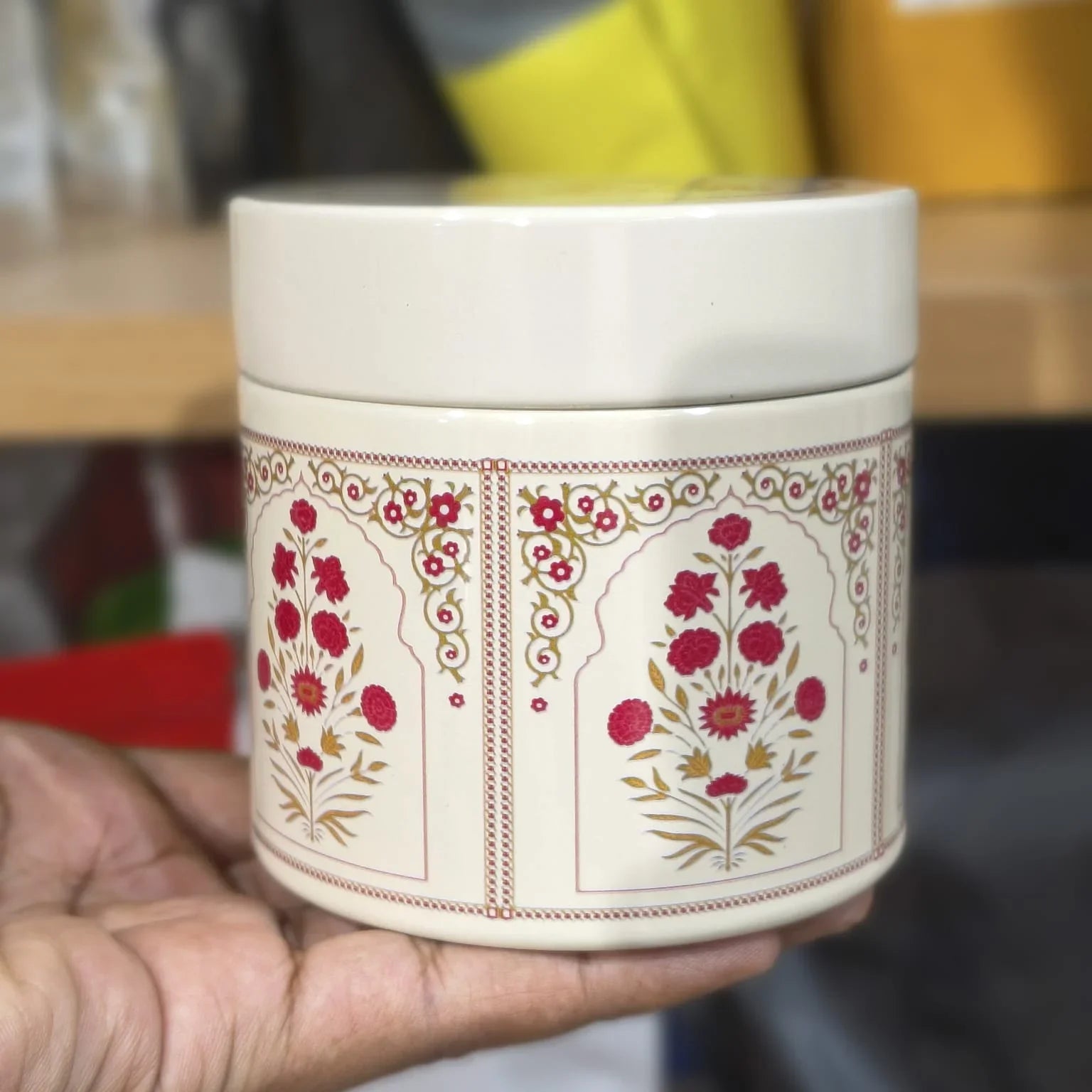 Hand holding a decorative ceramic container with floral patterns