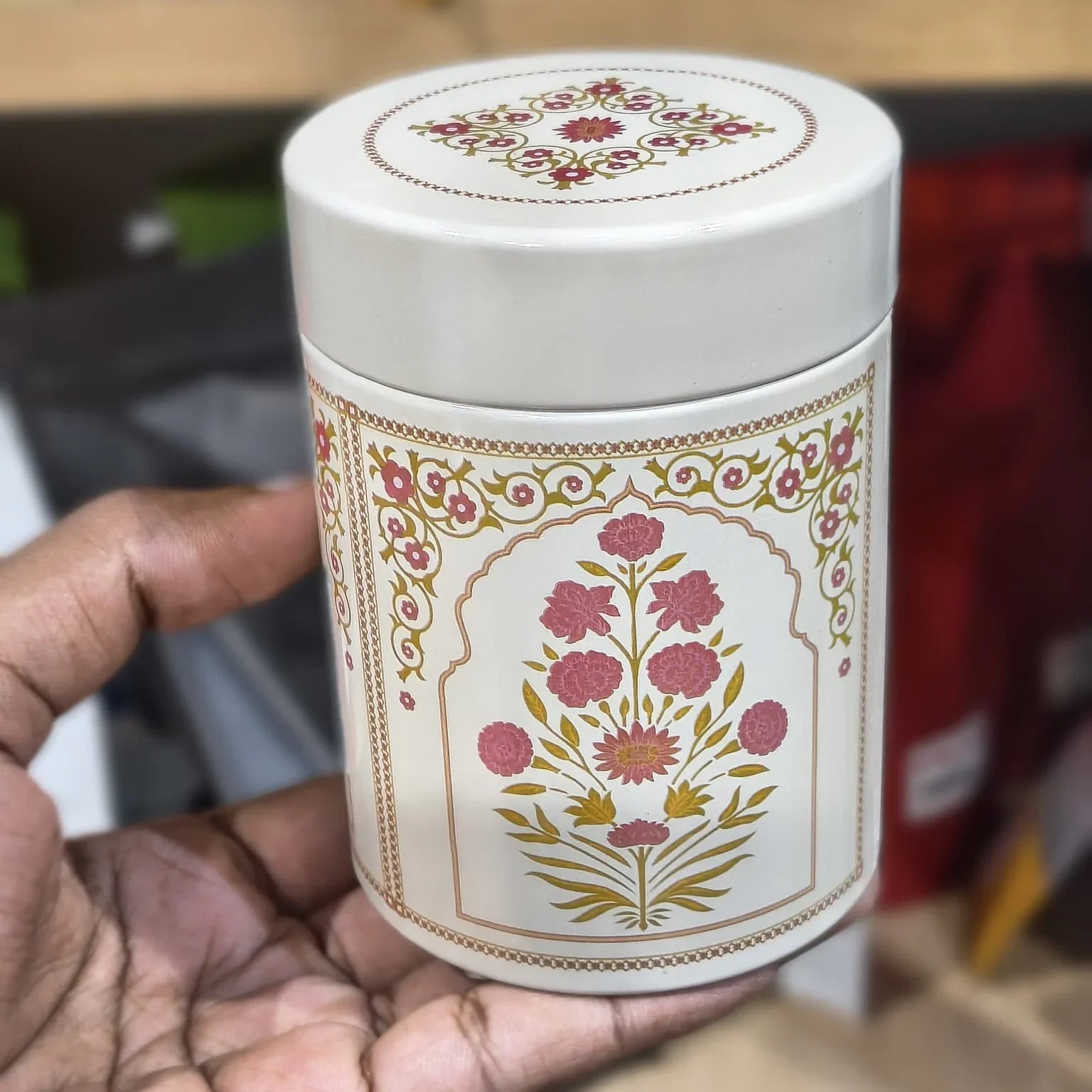 White cylindrical container with floral design held by a hand against a blurred background