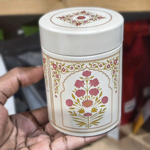 White cylindrical container with floral design held by a hand against a blurred background