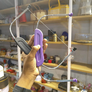 A hand holding a small bow saw with a purple handle and silver metal frame, set against a background of store shelves filled with various household items.