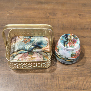 A decorative gold metal tray with a floral print and a matching lidded jar, displayed on a wooden tabletop.
