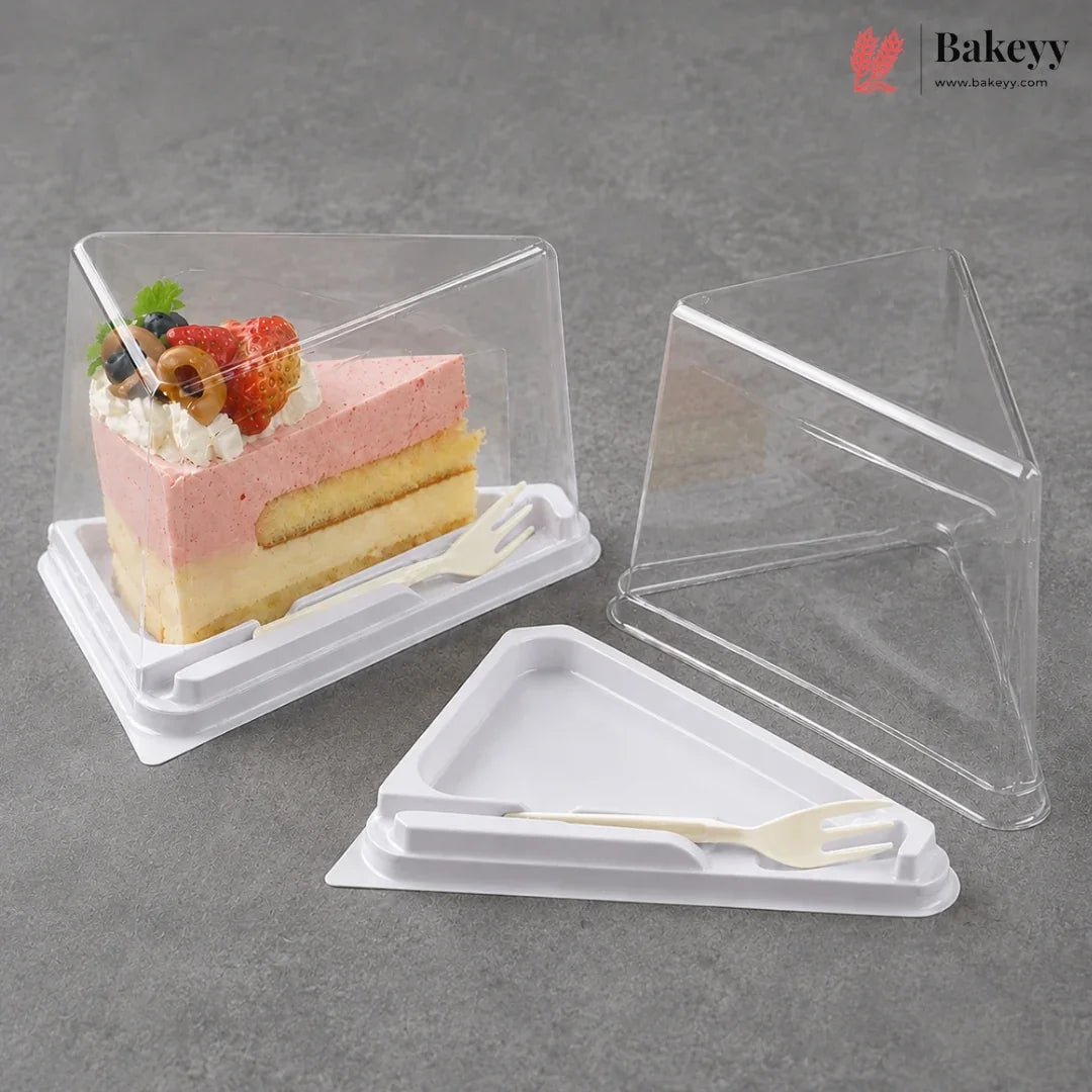 Clear plastic triangular cake box with a white base and small white plastic fork, shown both filled with a layered pink and yellow cake slice and empty on a gray surface. Bakeyy logo appears in the top right.