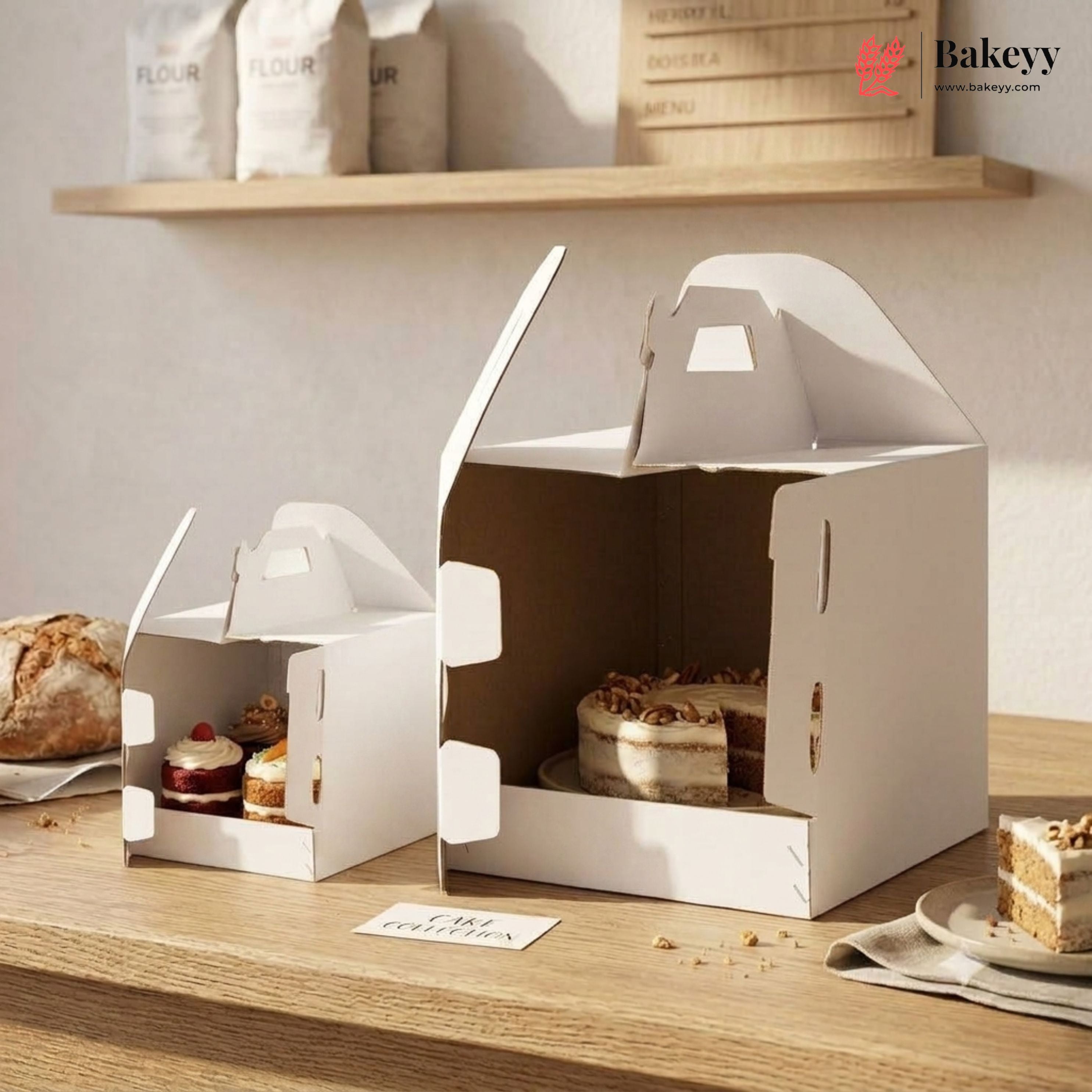 White cake boxes with baked goods on a wooden surface, featuring the Bakeyy brand.