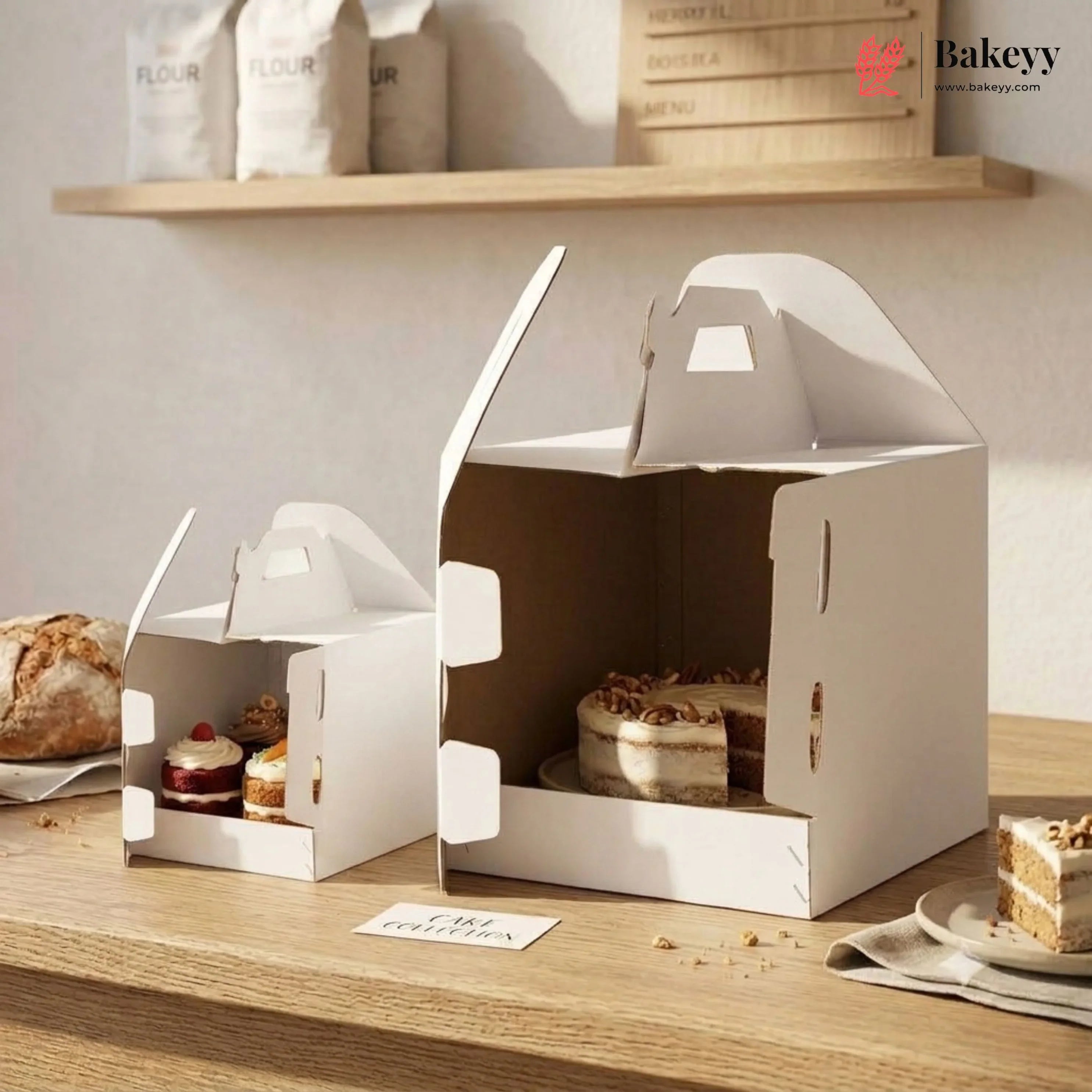 White cake boxes with baked goods on a wooden surface, featuring the Bakeyy brand.