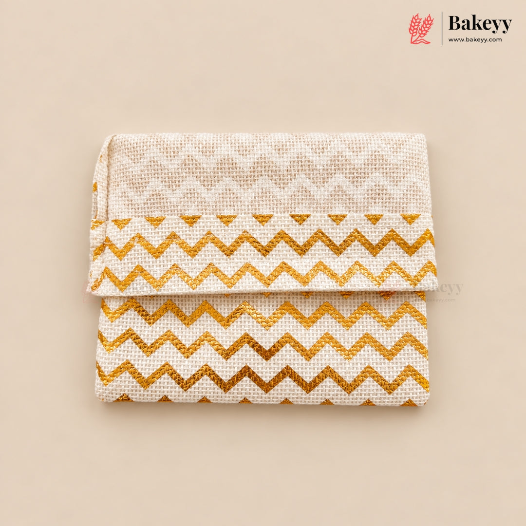 A folded fabric pouch or clutch with a cream woven texture, featuring a gold glitter chevron pattern on the lower half and a subtle cream geometric pattern on the top flap. The product is displayed on a solid beige background with the Bakeyy brand logo in the top right corner.