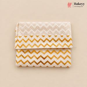 A folded fabric pouch or clutch with a cream woven texture, featuring a gold glitter chevron pattern on the lower half and a subtle cream geometric pattern on the top flap. The product is displayed on a solid beige background with the Bakeyy brand logo in the top right corner.