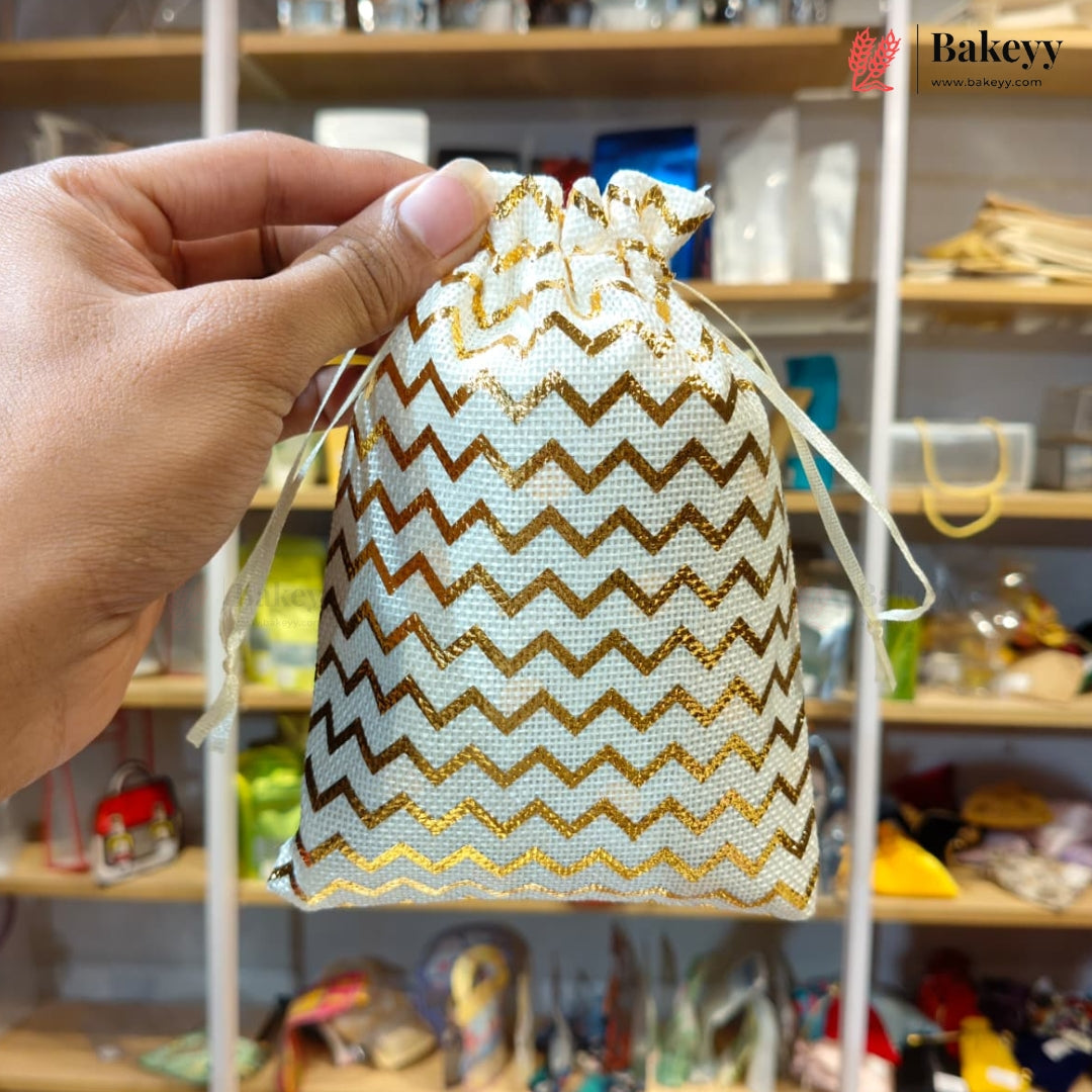 A hand holds a small drawstring pouch with a white and gold chevron pattern, set against a blurred background of shelves containing various items. A 'Bakeyy' brand logo is visible in the top right corner.