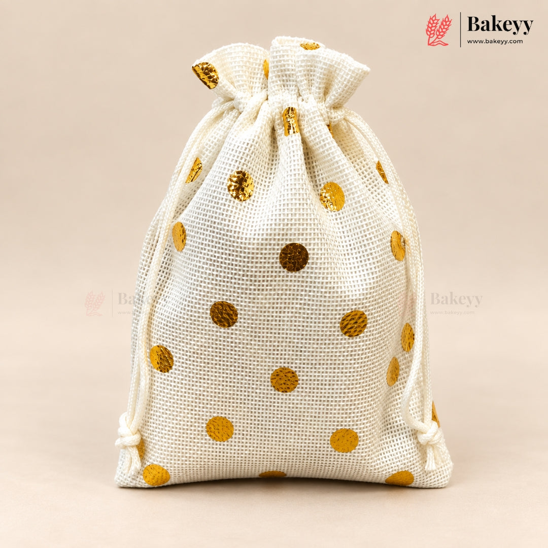An off-white burlap drawstring bag with metallic gold polka dots, shown on a solid beige background. The Bakeyy brand logo is visible in the top right corner.