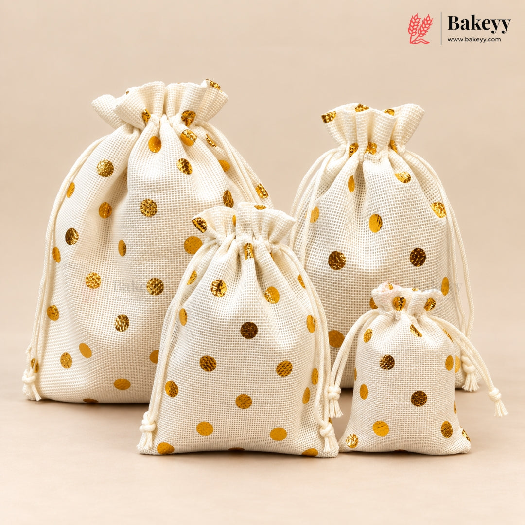 Four cream-colored cotton drawstring gift bags with metallic gold polka dots in different sizes, arranged on a solid beige background. The Bakeyy brand logo is visible in the top right corner.