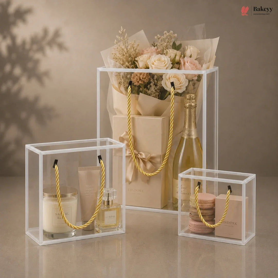 Clear display boxes with gold handles containing a bottle of wine, flowers, and other items on a neutral background.