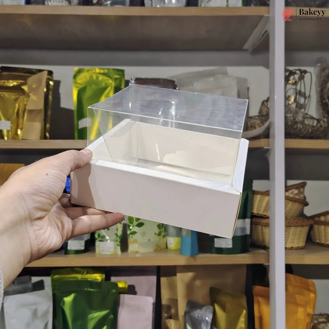 Hand holding a small white box with a clear lid against a blurred store shelf background